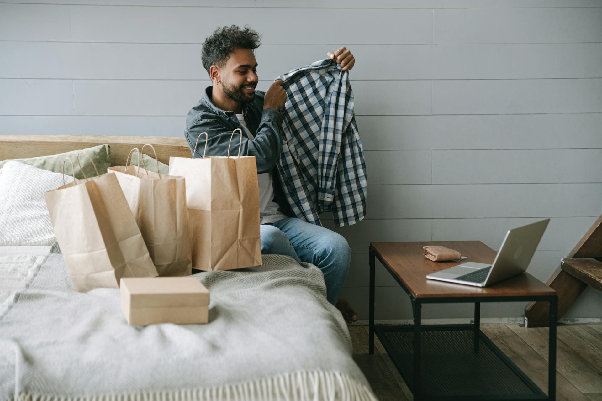 A man delightedly examines his new shirt after online shopping in a cozy room setting.