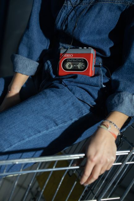 Close-up of a person in denim wearing a retro cassette player, capturing vintage fashion vibes.