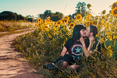 Couple Sitting in the Field of Sunflowers by the Country Road and Kissing