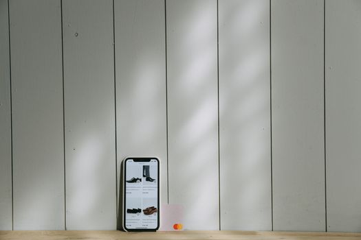 A smartphone and credit card sit on a wooden surface with soft lighting shadows.