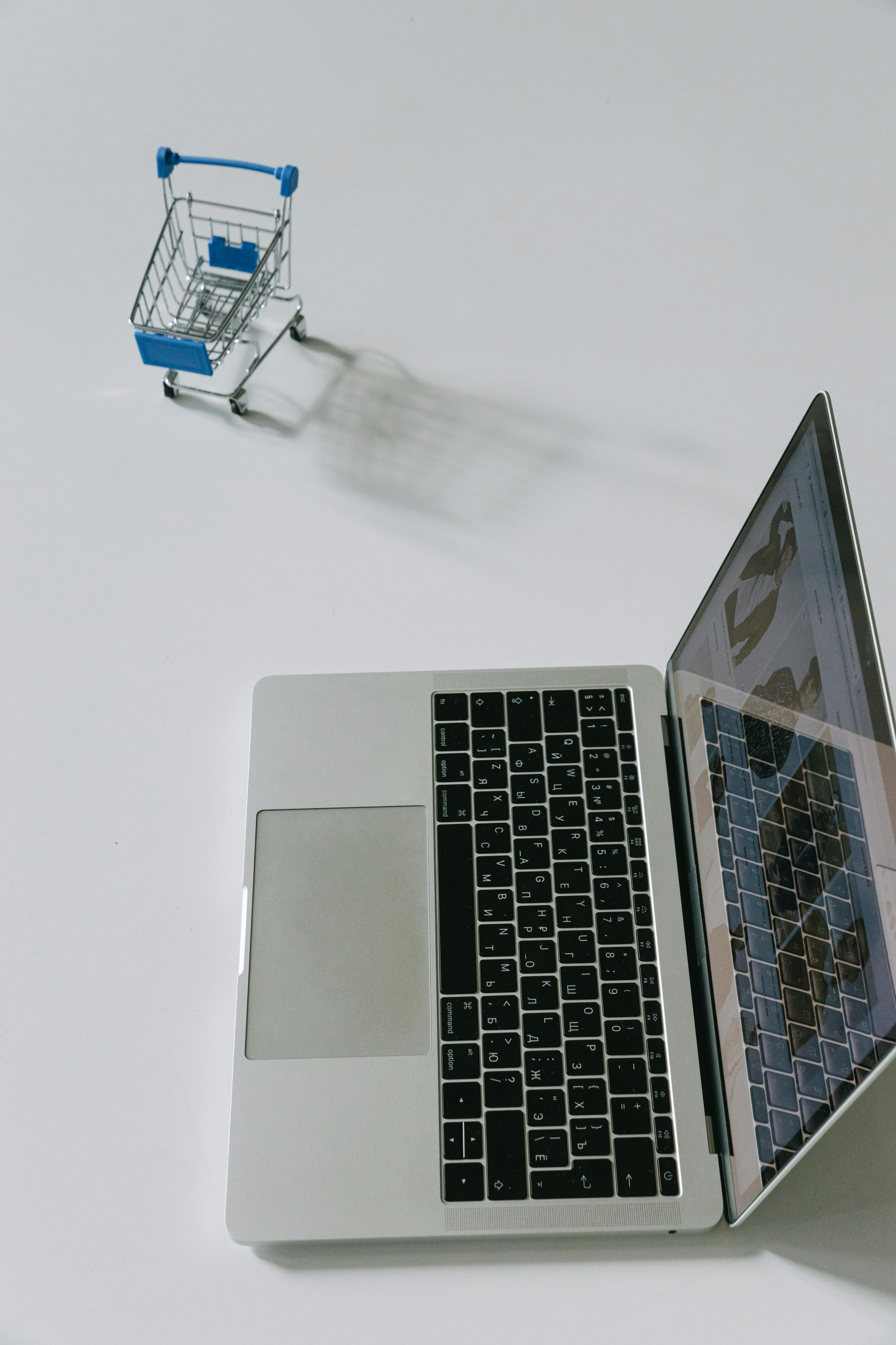 a laptop beside a miniature shopping cart