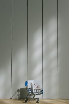 A small shopping cart casting a shadow on a panelled wall with sunlight.
