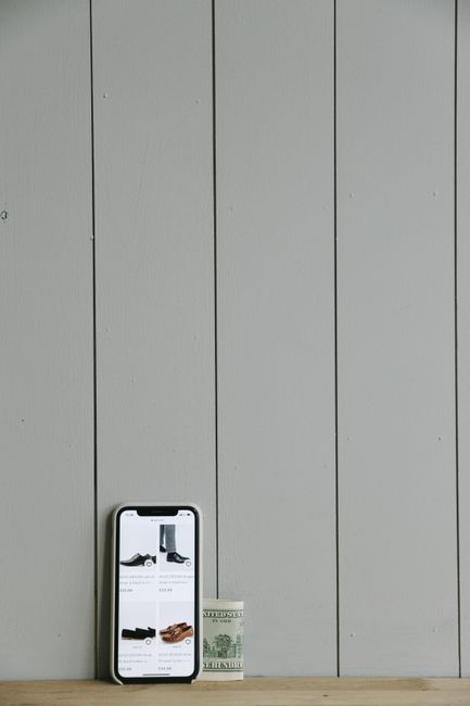A smartphone displaying online shopping apps beside cash on a wooden surface. A smartphone displaying online shopping apps beside cash on a wooden surface.
