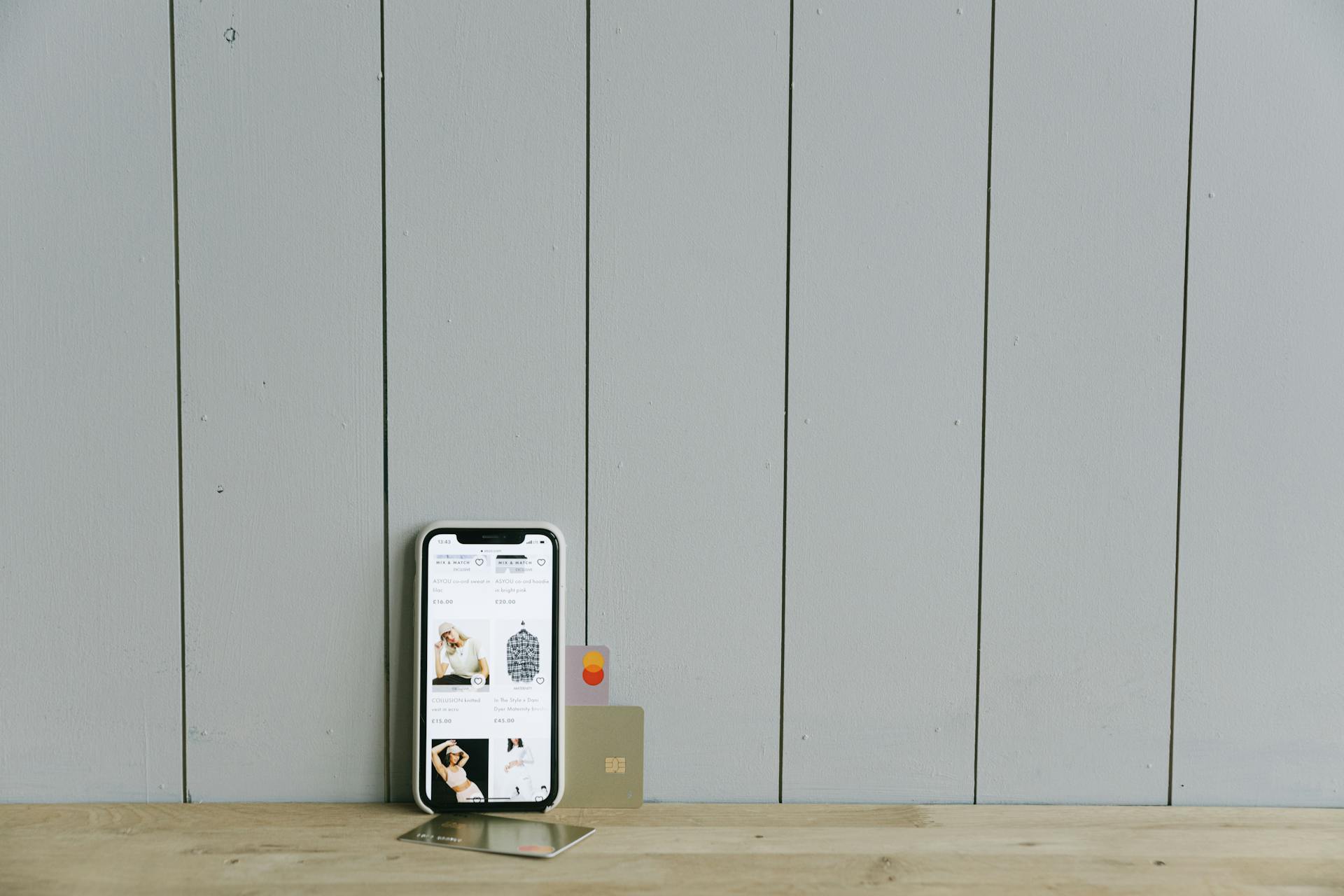 A smartphone displaying an ecommerce site with a credit card, set on a wooden surface, depicting online shopping.