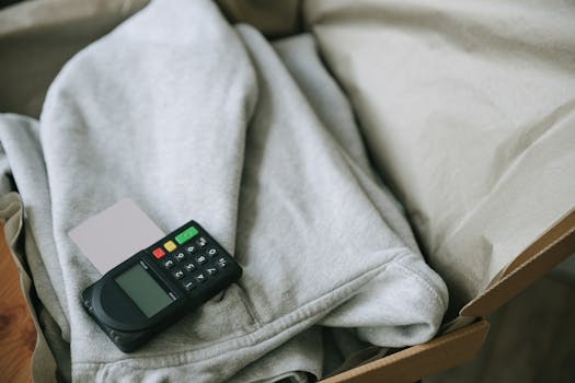 A payment terminal and card placed on folded clothing inside a shipping box, indicating e-commerce packaging.