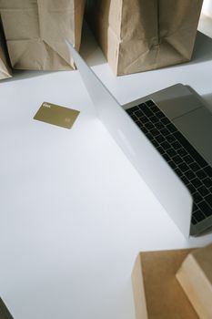 A laptop with a credit card, surrounded by paper bags, illustrating online shopping.