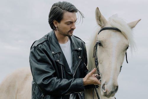 A Man in Black Leather Jacket Caring for a Horse