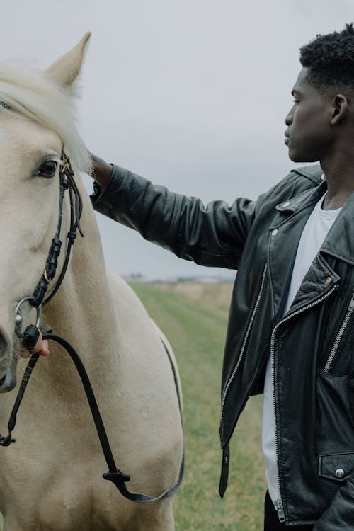 Man in Black Leather Jacket Standing Beside a White Horse
