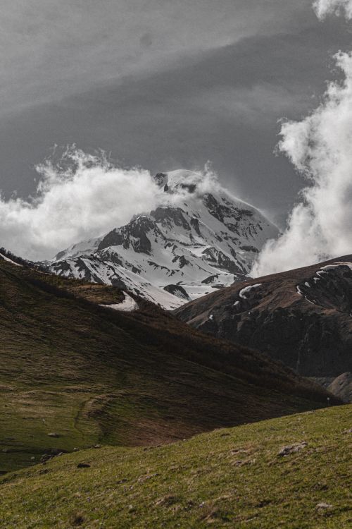 Free Breathtaking view of a snow-capped mountain peak enveloped by dramatic clouds in a vibrant landscape. Stock Photo