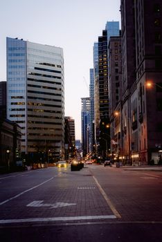 Dusk cityscape showcasing tall skyscrapers lining a bustling street, with glowing street lights and clear evening sky.