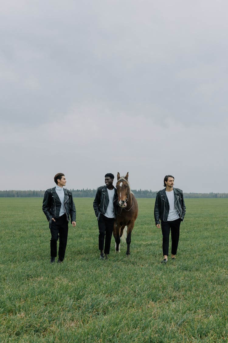 Men Walking On A Grassy Field With A Horse