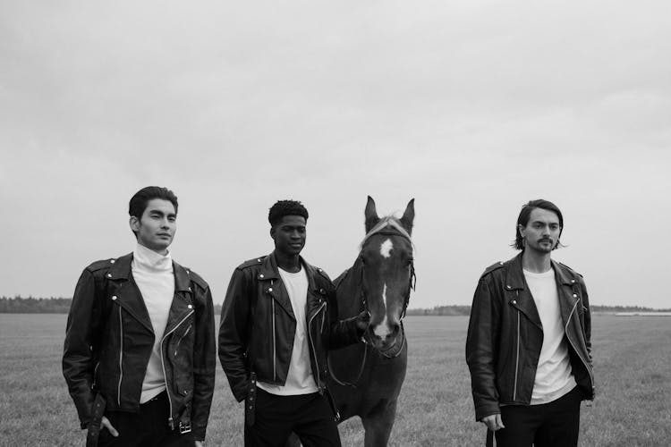 Grayscale Photo Of Men Walking On A Grassy Field With A Horse