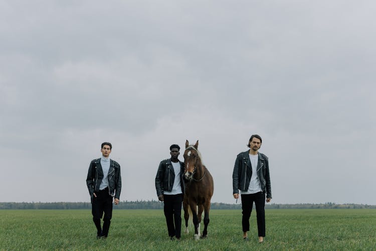 A Group Of Men Walking On A Grassy Field With A Horse