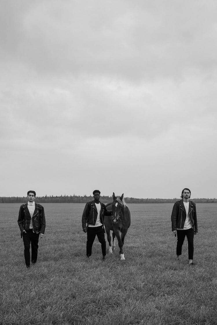 Grayscale Photo Of Men Walking On A Grassy Field With A Horse