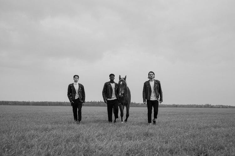 Grayscale Photo Of Men Walking On A Grassy Field With A Horse