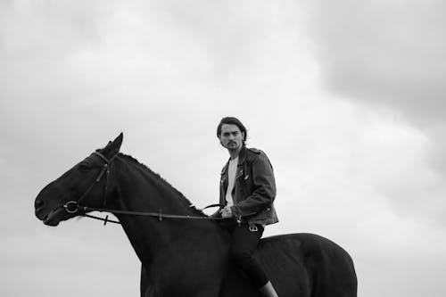 Grayscale Photo of Man Riding a Horse