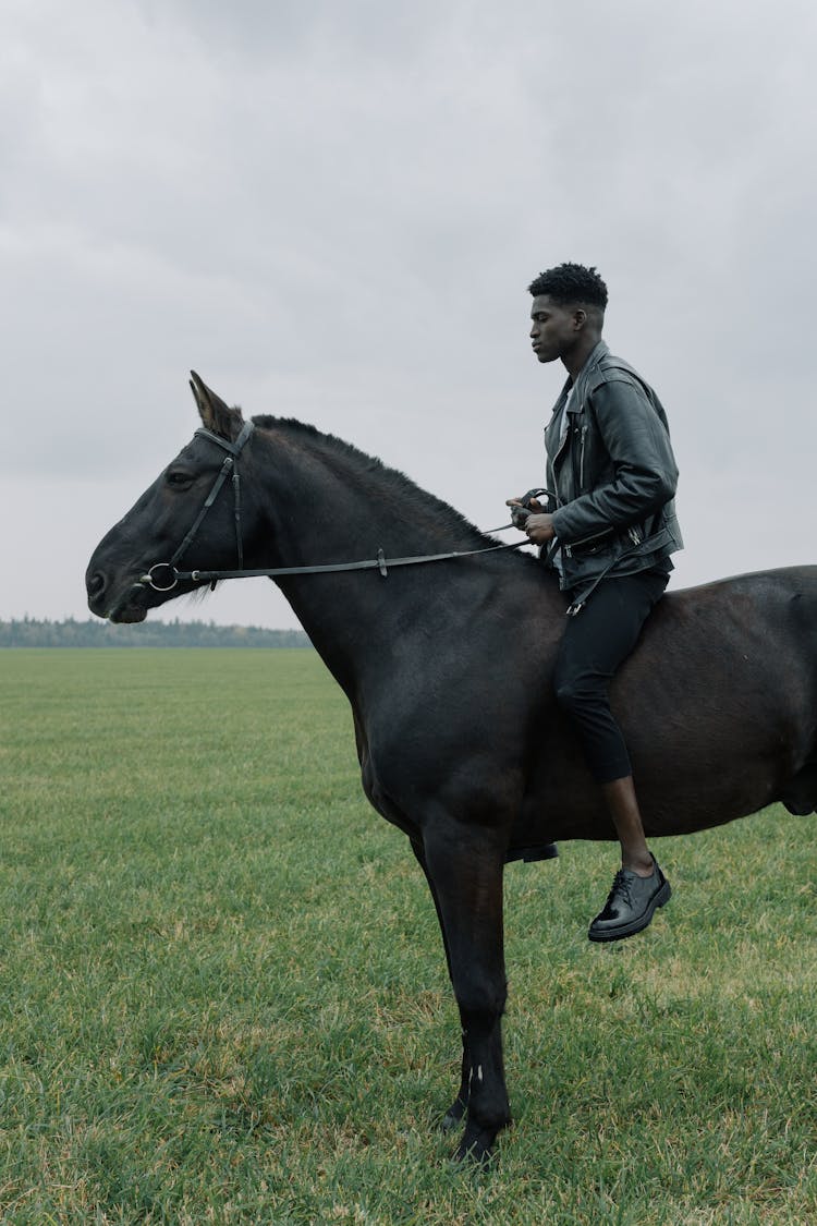 A Man Riding A Black Horse On A Grassy Field