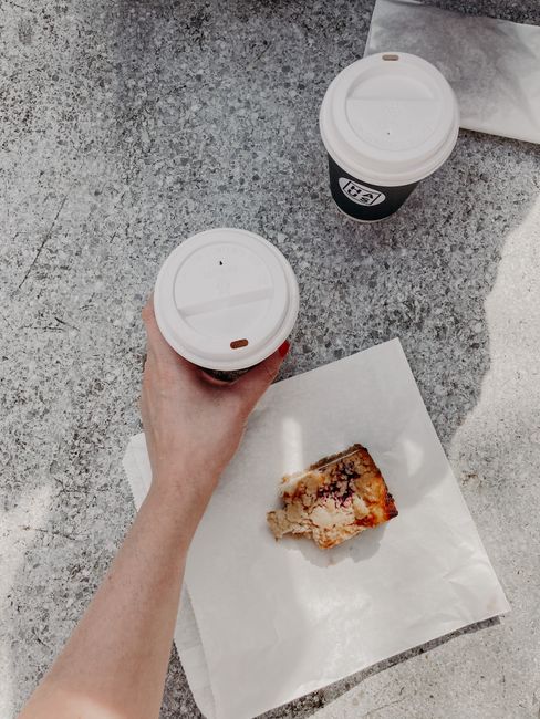 From above of crop anonymous female drinking takeaway coffee and eating sweet pie placed on white bag white having break on street on sunny day