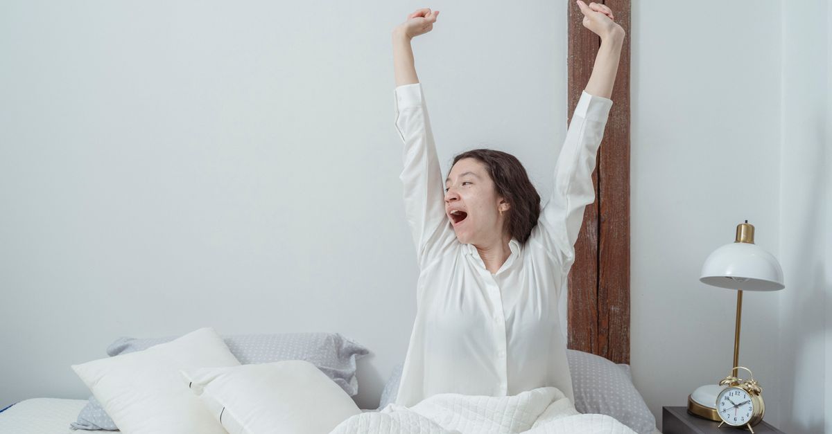 Vrouw rekt zich gapend uit in een wit bed