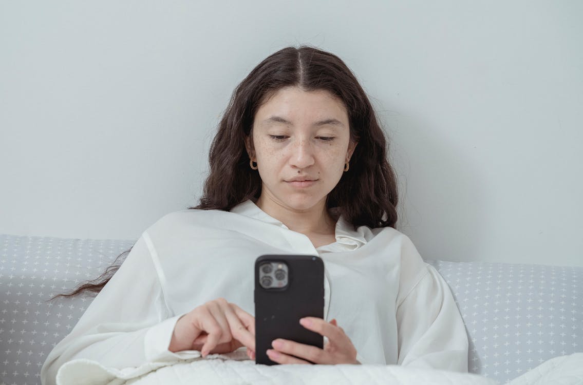 Free Young woman using smartphone while resting on bed Stock Photo