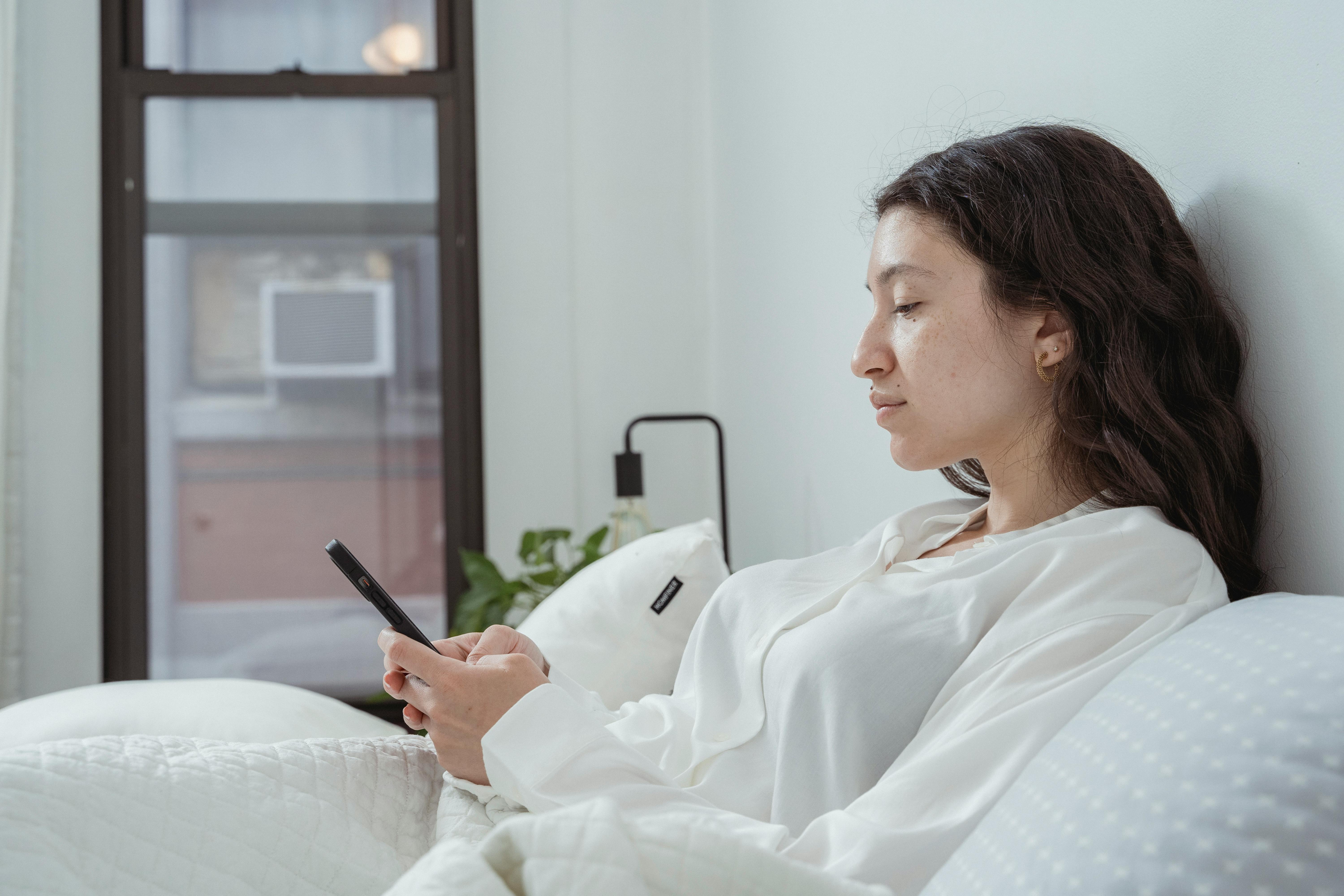 calm woman resting on bed with smartphone