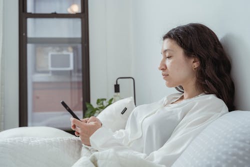 Calm woman resting on bed with smartphone