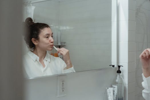 Adult woman brushing teeth, reflected in bathroom mirror. Clean and minimal style.
