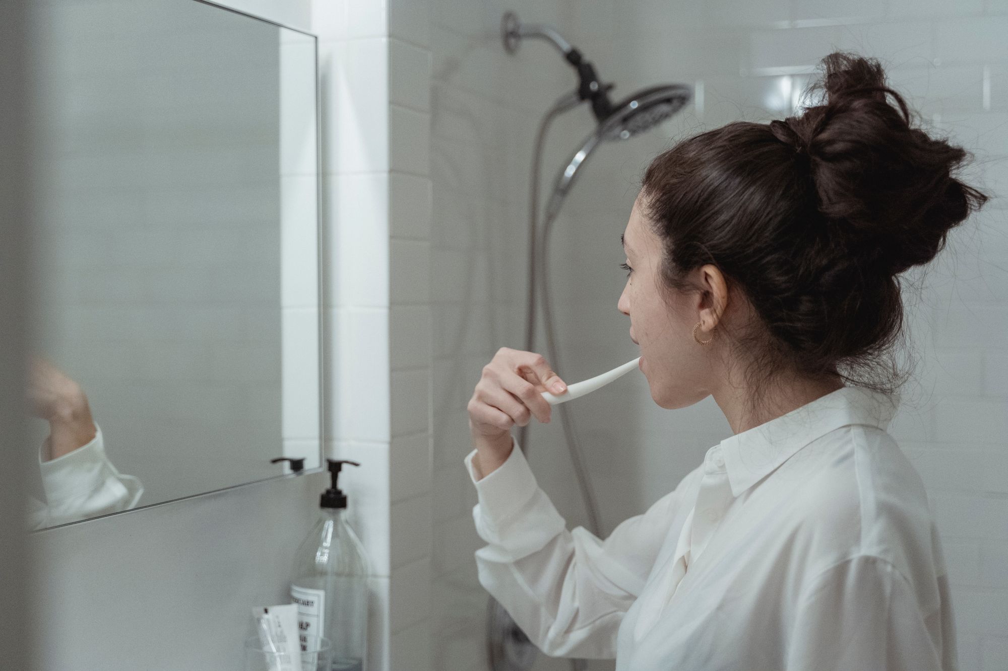 Woman brushing her teeth in a bright modern bathroom as part of a consistent daily oral-care routine