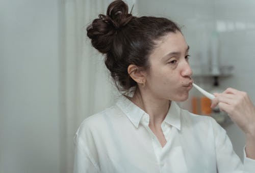 Woman in White Long Sleeves Brushing Her Teeth