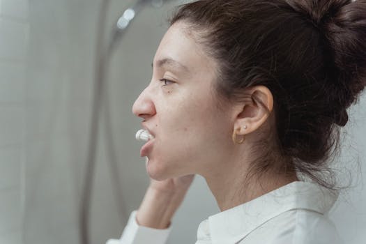 Side view of a woman with hair bun brushing teeth as part of her hygiene routine indoors.