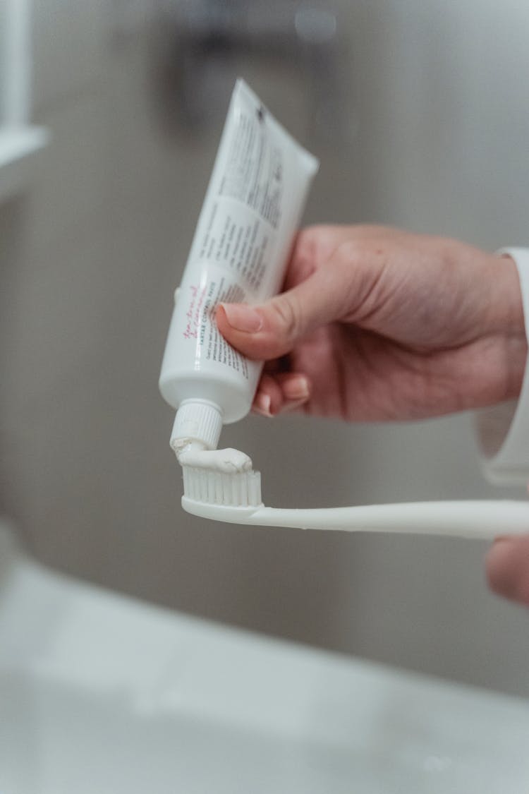 Person Putting Toothpaste On Toothbrush