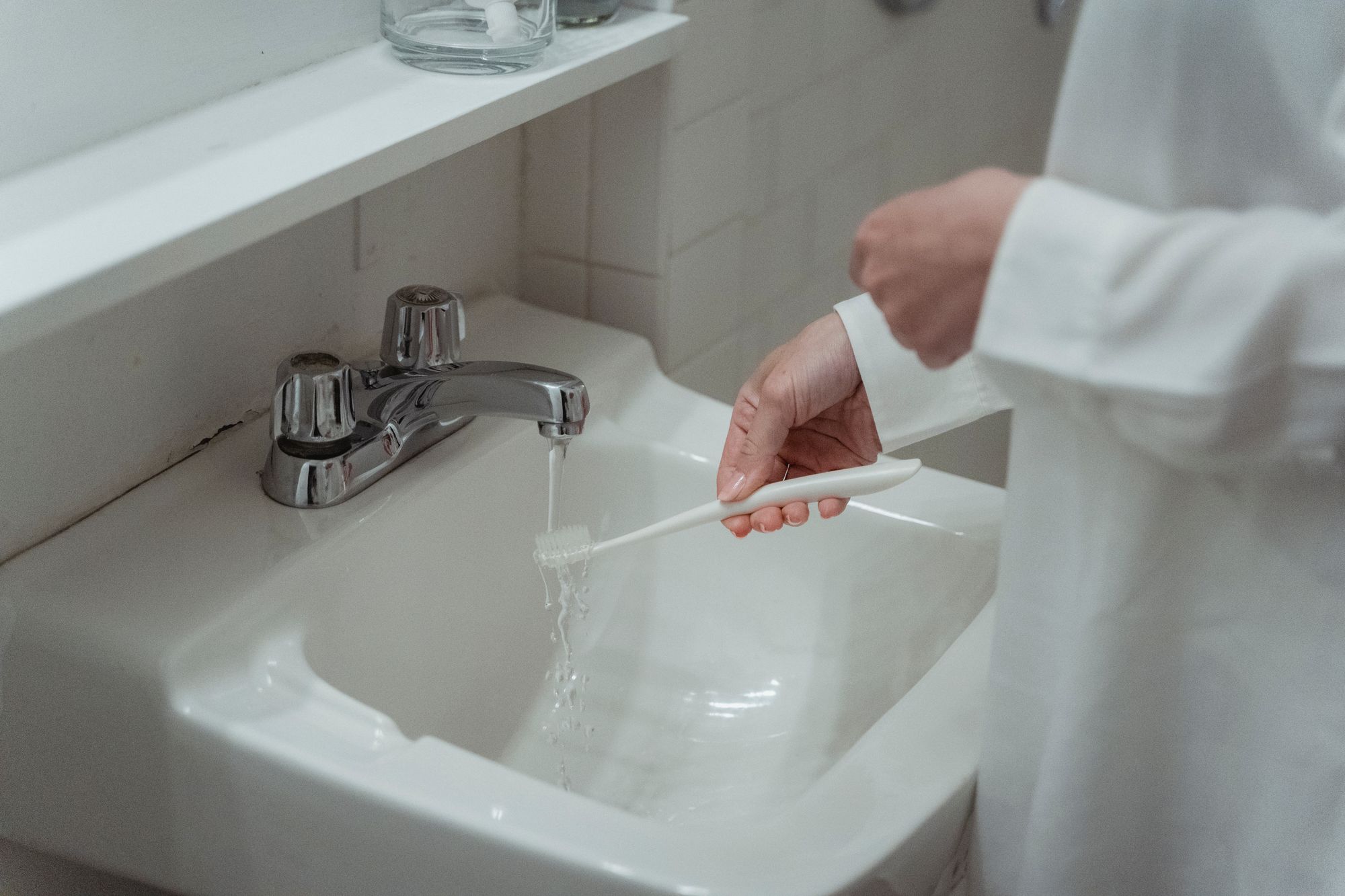 Hands rinsing a toothbrush beneath a bathroom faucet as part of a clean oral-care routine