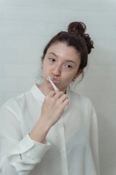 Young woman in a white shirt brushing teeth as part of her morning hygiene routine.