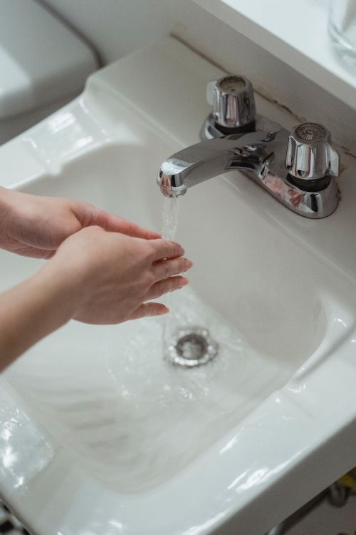 Free Close-up of hands being washed under a modern stainless steel faucet in a white washbasin. Stock Photo