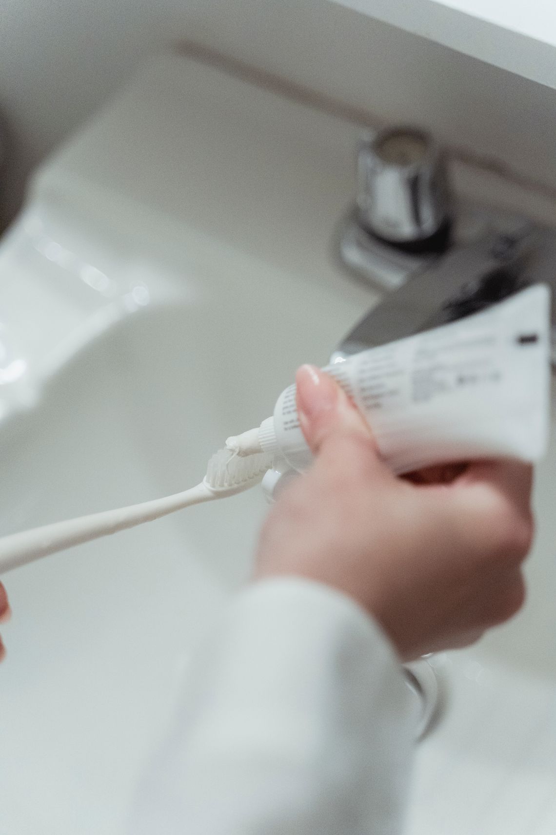 Hands holding a toothbrush and toothpaste beside a bathroom sink
