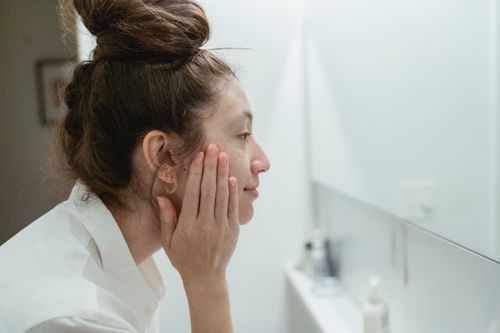 Free Profile view of a woman touching her face and reflecting in the bathroom mirror. Stock Photo