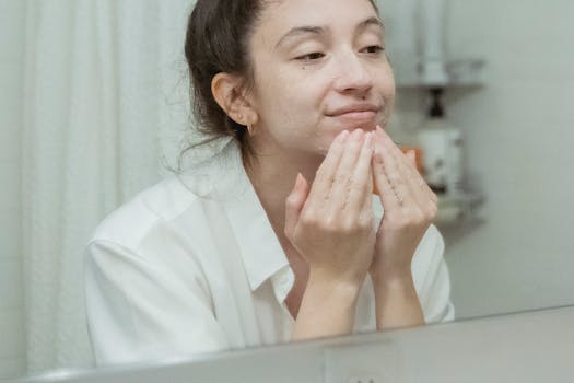 A woman applies facial cream, enjoying her skincare routine in front of a bathroom mirror.