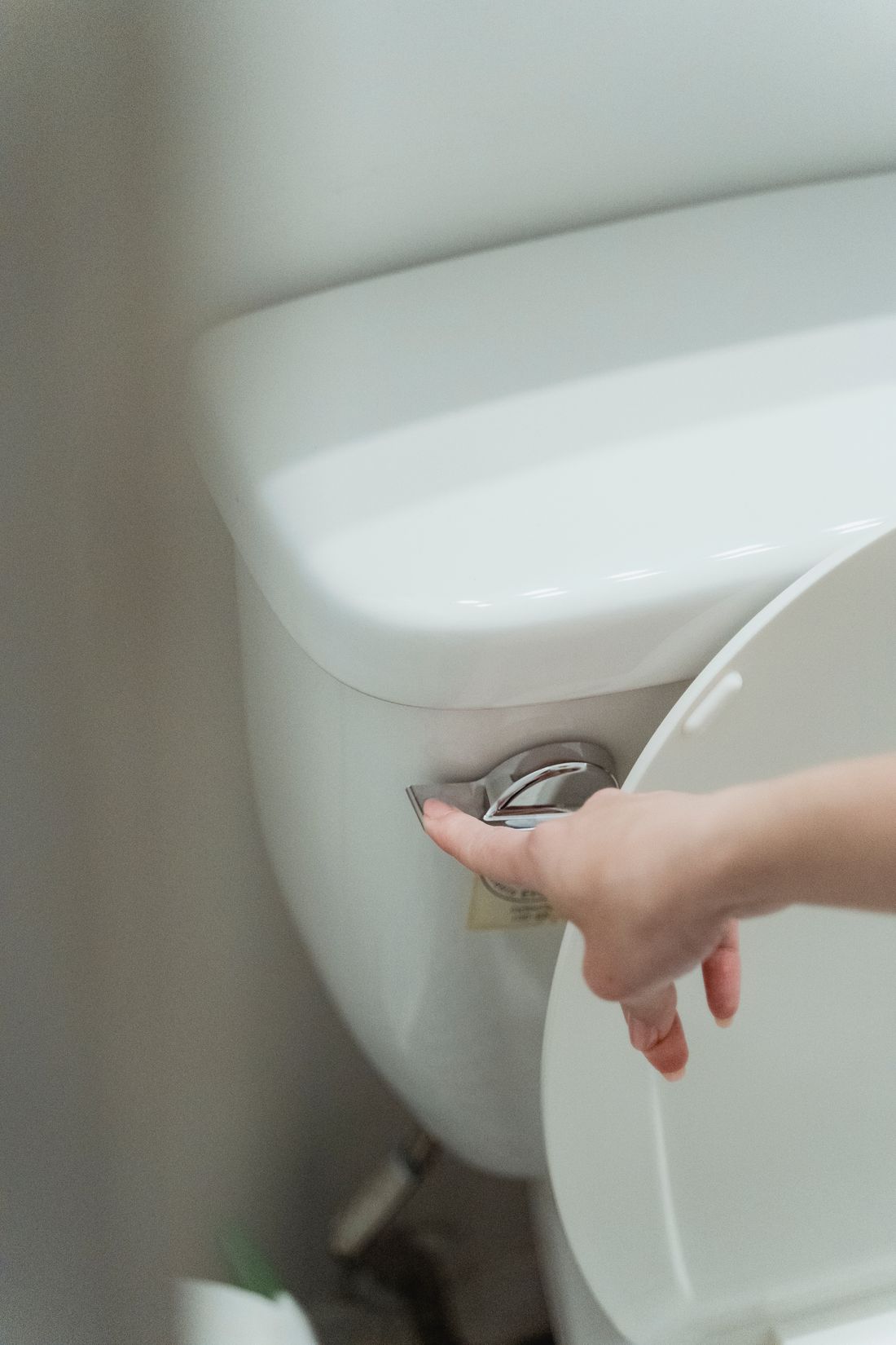 Plumber servicing toilet internals with the tank open and hands working inside