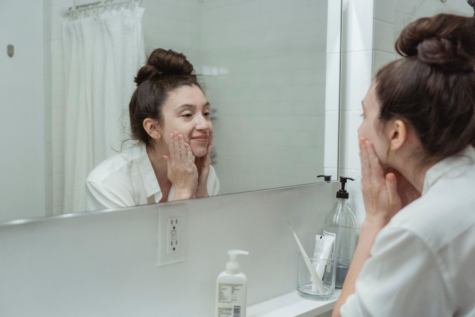 Woman applying facial care product while looking into a bathroom mirror