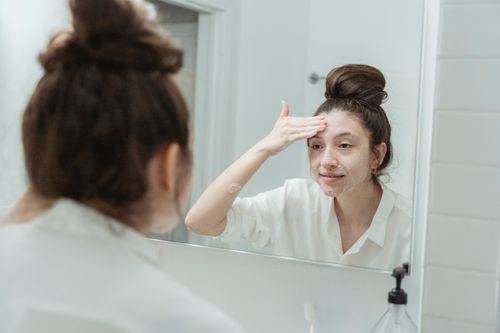 Free Young woman applying facial cream while looking at her reflection in the bathroom mirror. Stock Photo