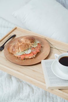 Enjoy a cozy breakfast in bed with a croissant sandwich and coffee.