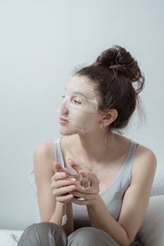 Young woman relaxing with a facial mask and cup of tea, embodying self-care.