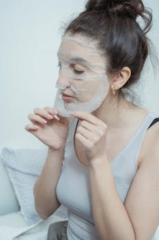 Woman relaxing indoors while applying a skincare face mask for rejuvenating beauty treatment.