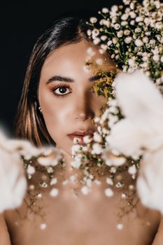 A captivating portrait of a woman half-visible behind delicate flowers, showcasing elegance and beauty.