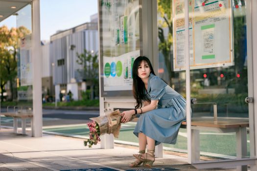 Woman in a Blue Dress with a Pink Flower Bouquet Sitting on at a Tram Stop
