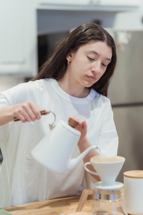 Woman with Long Hair and White T-shirt Pouring Water from a White Kettle
