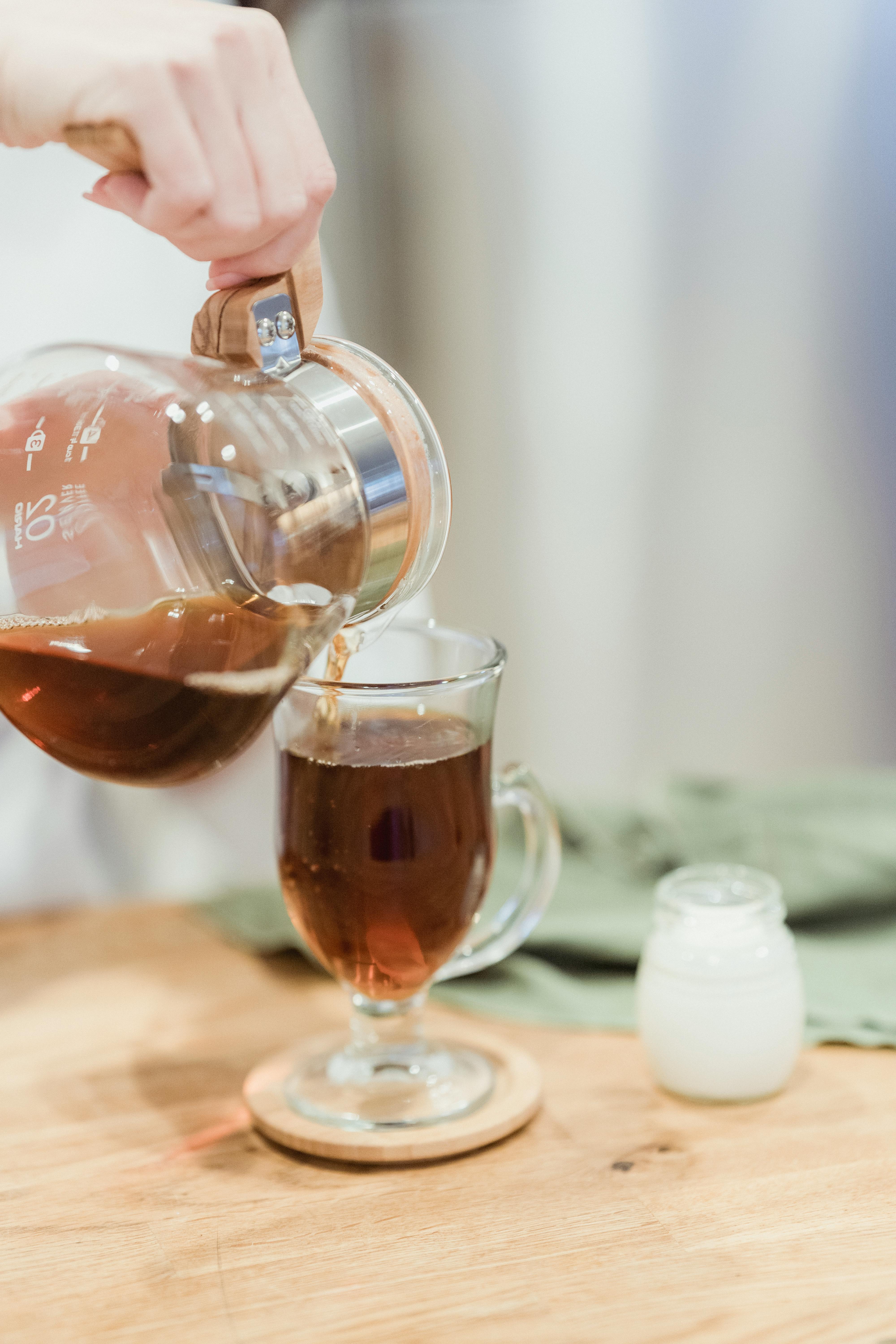 A close-up shot of tea being poured into a glass mug on a wooden surface.