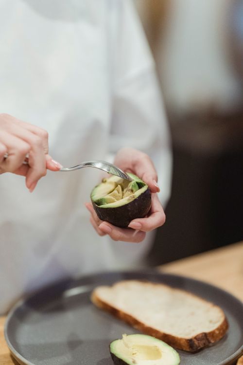 Free A person scooping avocado onto toast, ready to make a healthy meal. Stock Photo