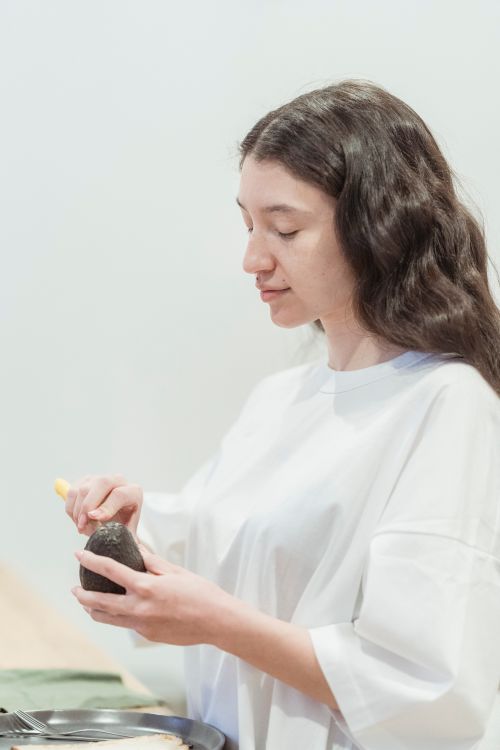 Free Young woman in white shirt preparing an avocado in a bright, minimalist kitchen. Stock Photo