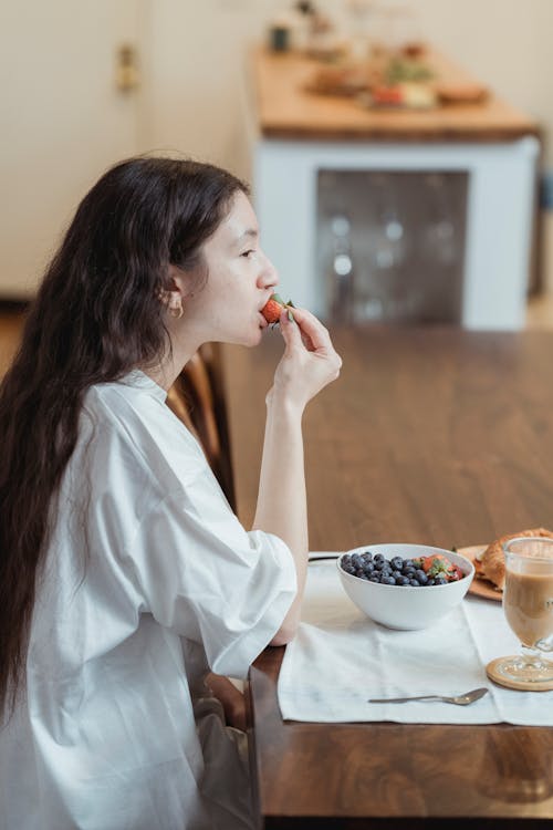 Woman in White Shirt Eating Strawberry